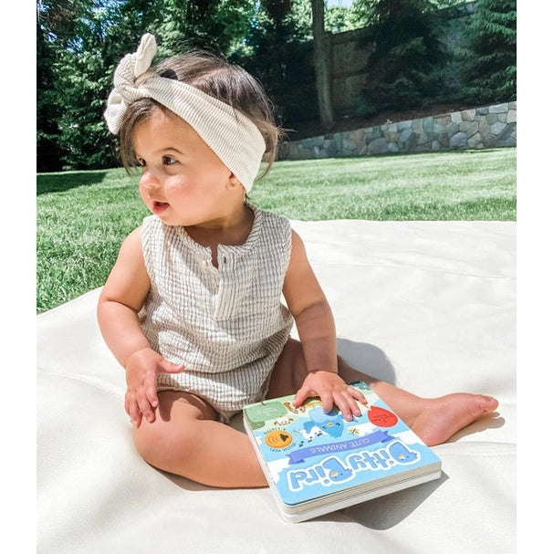 Ditty Bird Sound Book Touch The Cute Animals USB-C Rechargeable; baby girl sits outdoors on a blanket, touching the book.