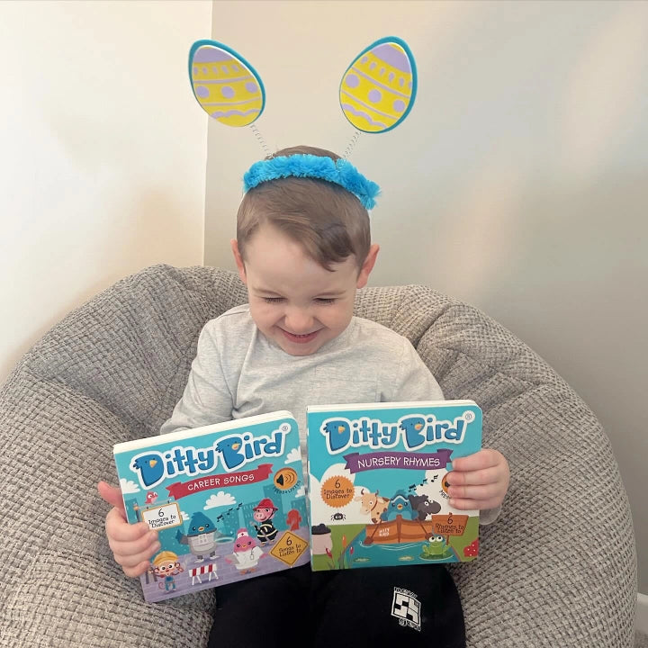 Ditty Bird Sound Book When I Grow Up Career Songs USB-C Rechargeable—smiling toddler holds a two-book set on a cozy bean bag.