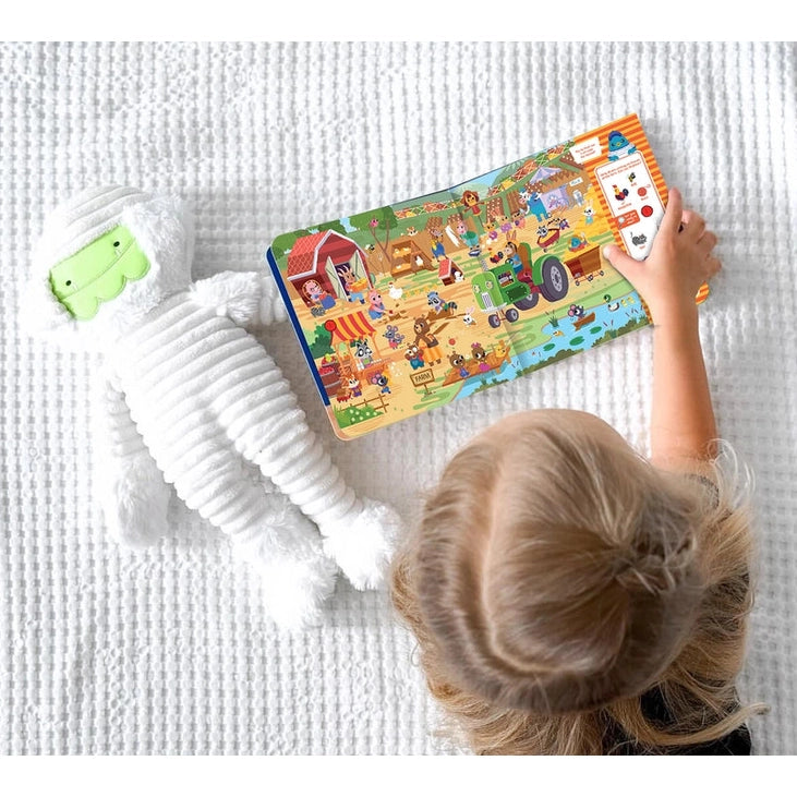 Ditty Bird Sound Book Where's Ditty Bird USB-C Rechargeable; child taps colorful pages on a plush white rug.