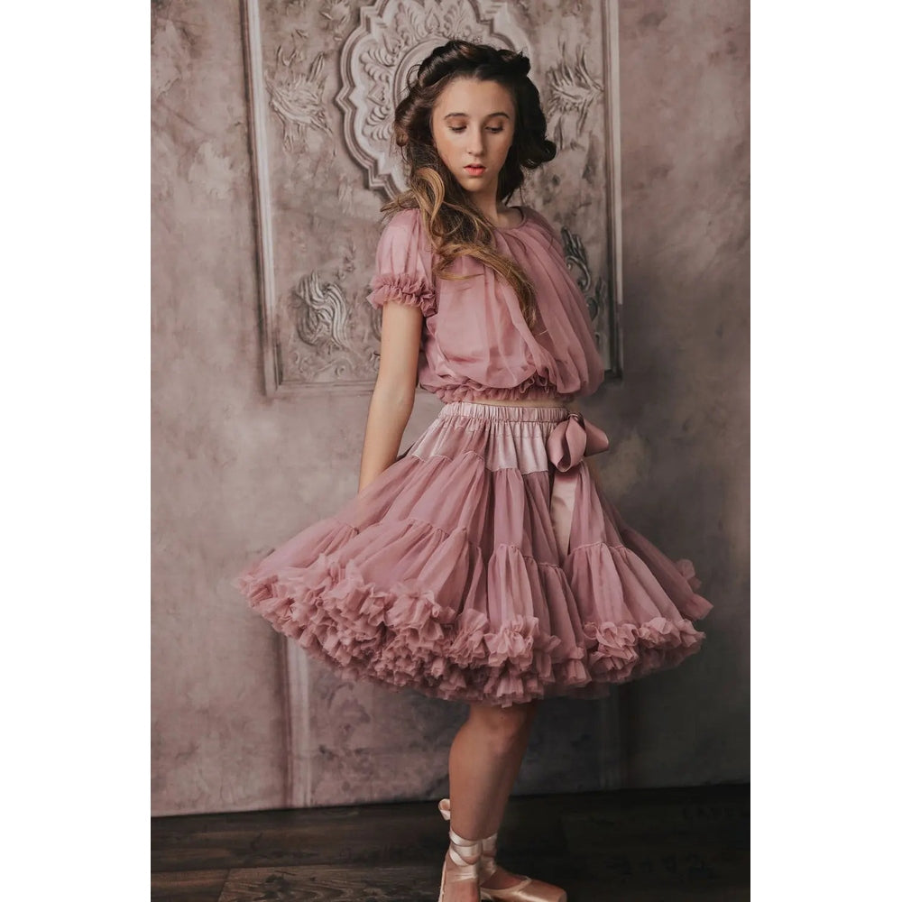 Dolly by Le Petit Tom Frilly Princess Top Mauve; girl twirls in a sheer, layered mauve top with puff sleeves and bow.