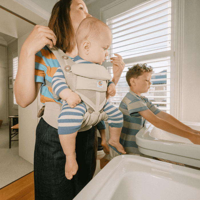 ERGOBABY Omni Classic Mesh Baby Carrier Natural Beige worn by a mother carrying a baby in front, with padded straps visible.