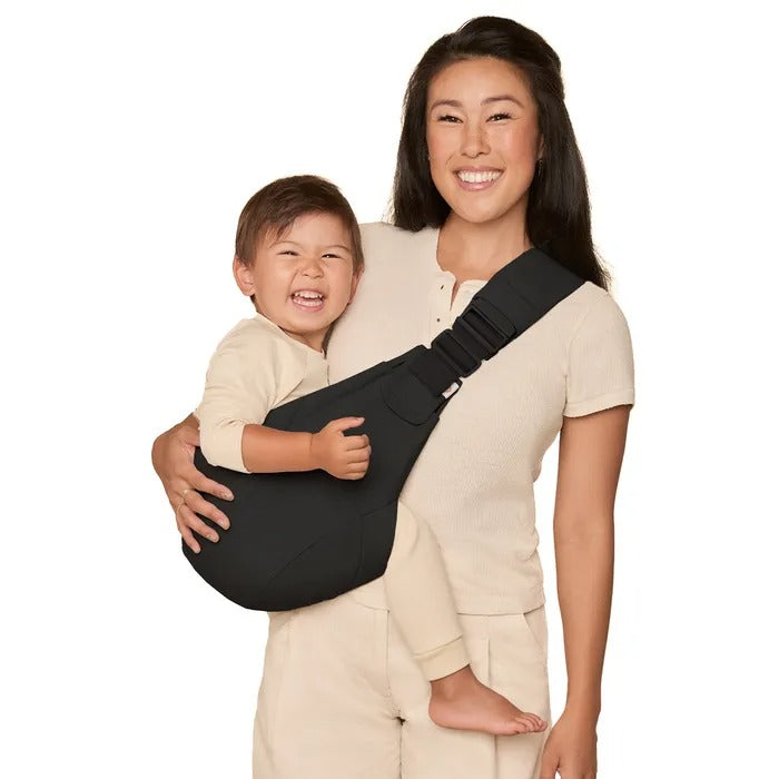 ERGOBABY Upsie Sling Carrier black being worn by smiling mom with toddler secured on her chest.