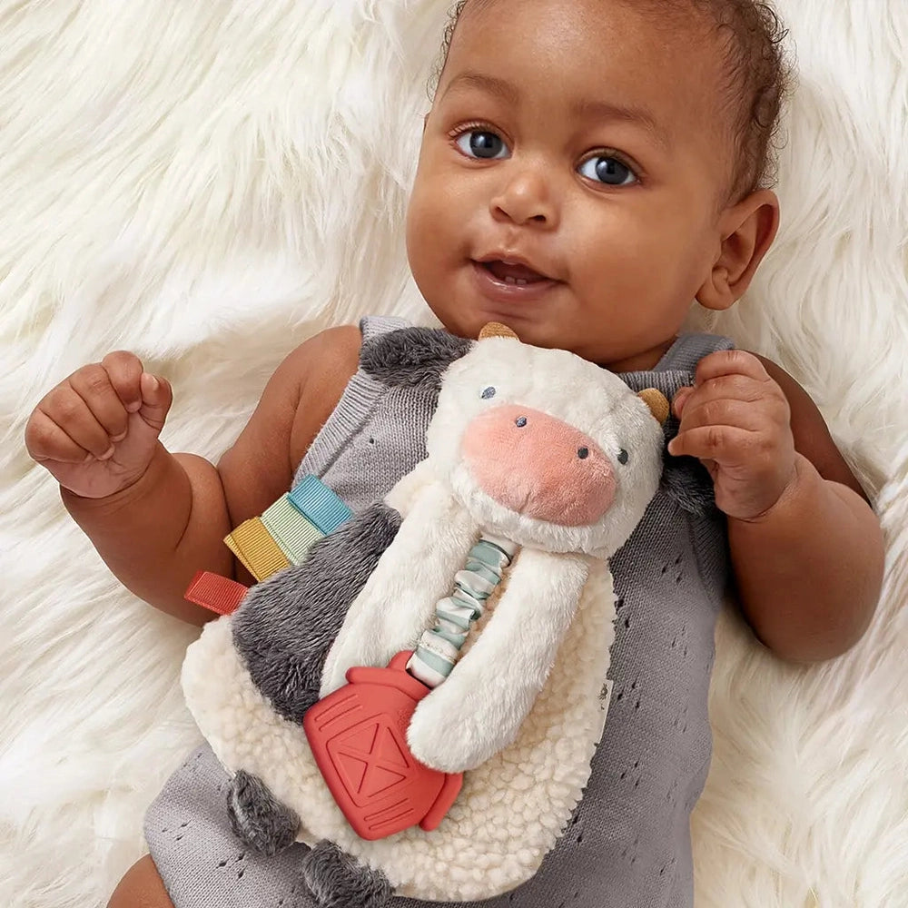 Itzy Ritzy Lovey plush and teether toy; gray white cow with rainbow ribbons and red teether for babies