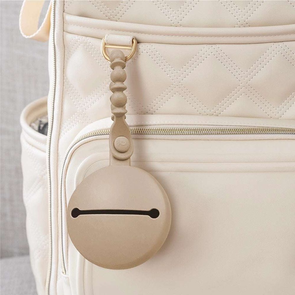 Itzy Ritzy Paci Pod beige pacifier holder with round pod clipped to quilted bag