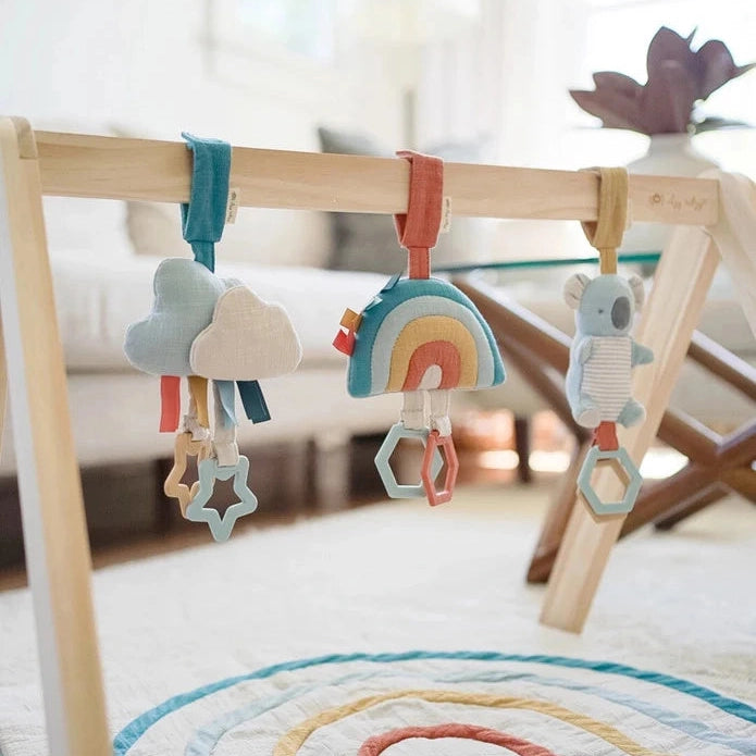 Itzy Ritzy JingleB Attachables: 3 pastel plush travel toys with cloud, rainbow and bear on a wooden baby gym