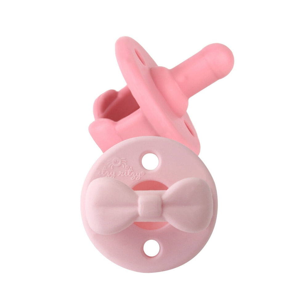 Itzy Ritzy Sweetie Soother Pacifier Sets 2 Pack 0M+ in pink, featuring a bow-tied pacifier shield and clip.