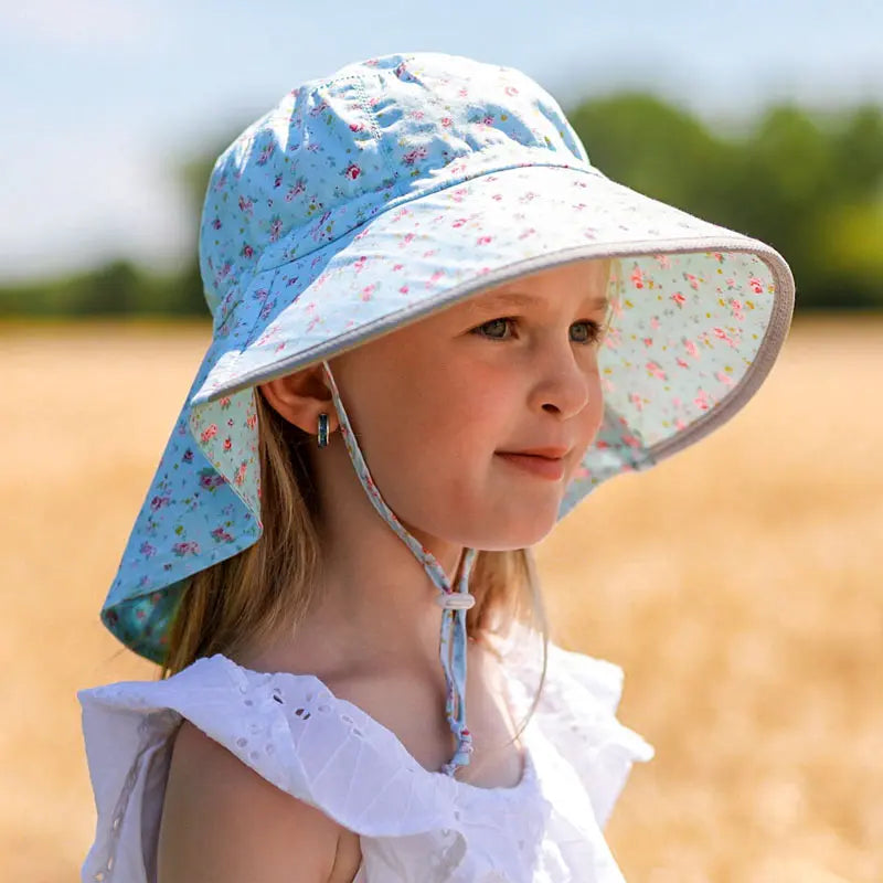 Jan & Jul Kids Cotton Adventure Hat Retro Rose worn by a girl in a sunlit field; blue floral print, wide brim, chin strap.