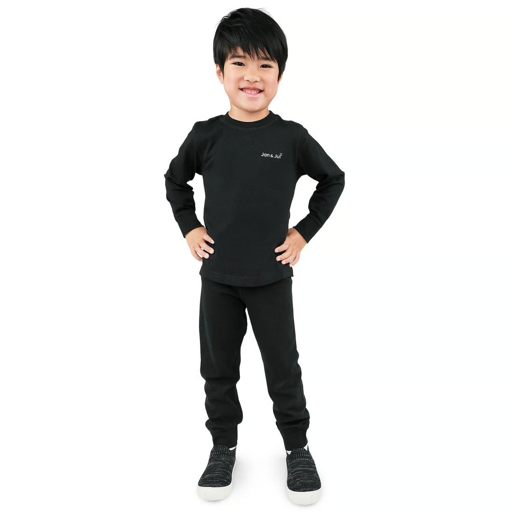 Jan & Jul Kids Cotton Blend Base Layer Tops Black worn by a smiling child in a black base layer set with hands on hips