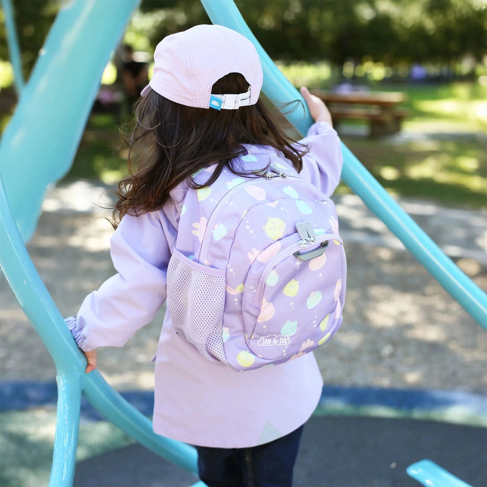 Jan & Jul Kids Mini Backpack in lavender with pastel planet print, worn by a child climbing a blue playground frame, featuring a mesh side pocket.