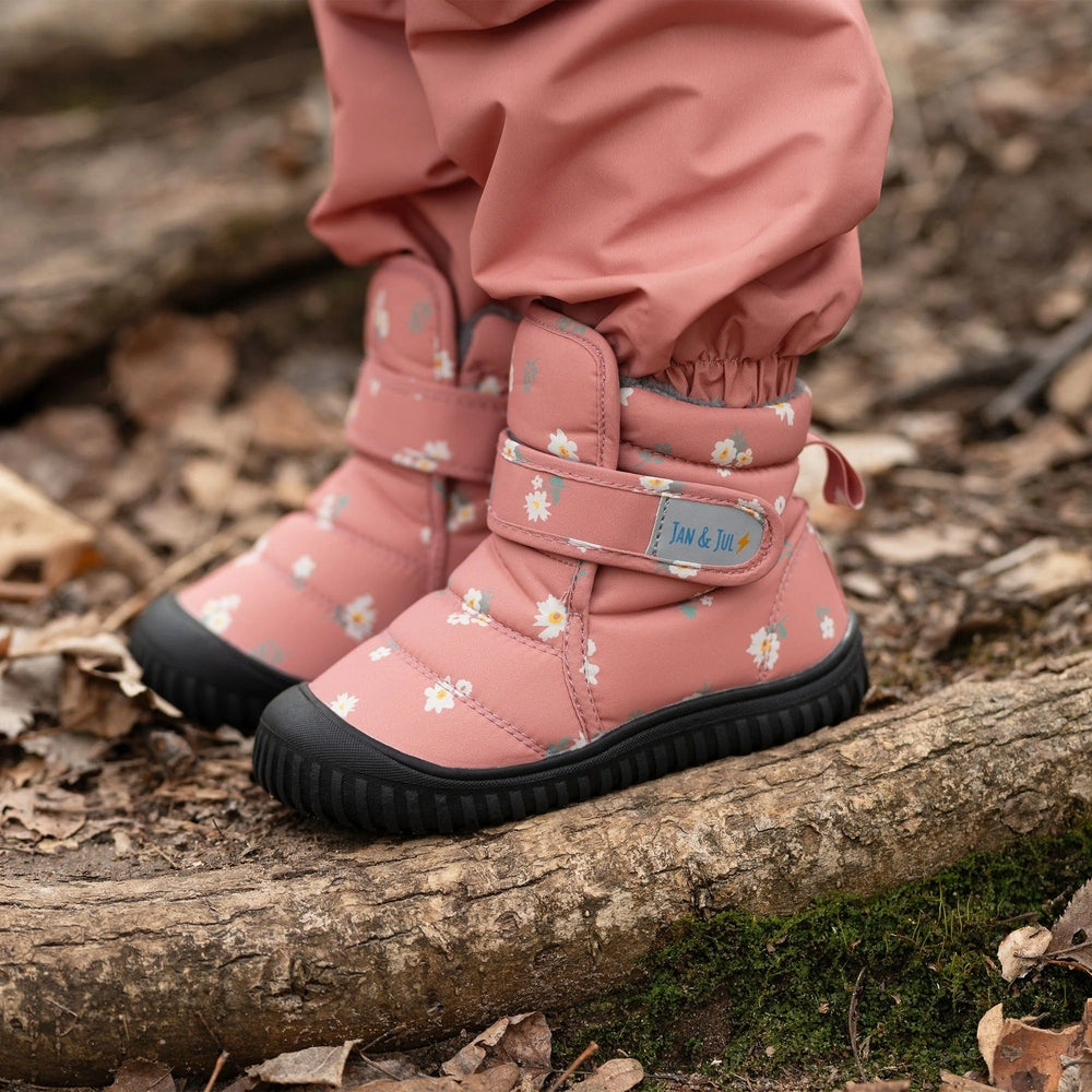 Jan & Jul Toasty Dry Booties Apricot Flower worn by toddler standing on a log, pink floral boots with Velcro straps.