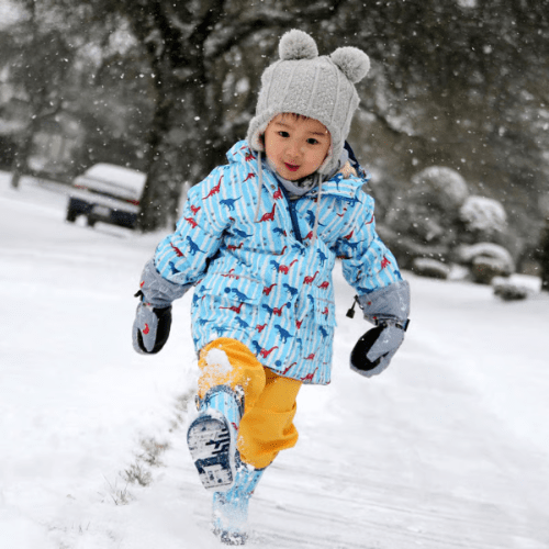 Jan & Jul Waterproof Cozy Dry Rain Pants Yellow; child runs through snow wearing bright yellow rain pants.