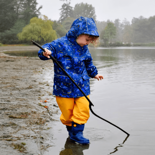 Jan & Jul Waterproof Cozy Dry Rain Pants Yellow worn by a child wading through shallow lakeside water in bright yellow rain pants