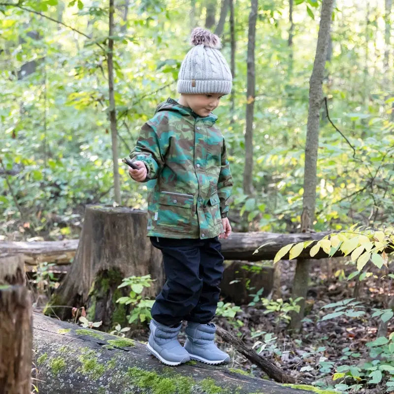 Toddler wearing JAN & JUL Waterproof Puddle Dry Rain Pants Black steps along a mossy forest log, ready for wet days.