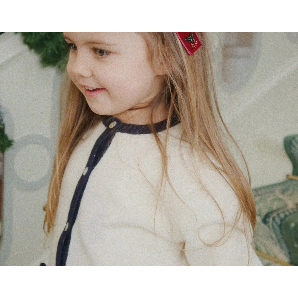 Konges Slojd Alette Cardigan Etoile worn by a smiling toddler in a cream knit with navy trim and buttons.
