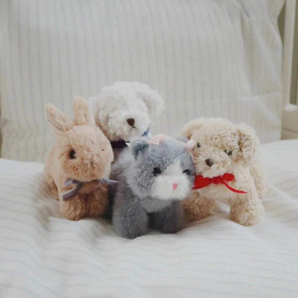 KONGES SLOJD Baby Animals plush set of four soft stuffed toys resting together on a striped bed, with ribbons.