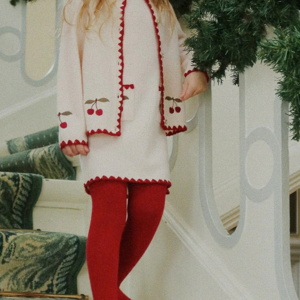 Konges Slojd Collette Cardigan Off White worn by a child with cherry embroidery and red trim by a staircase.