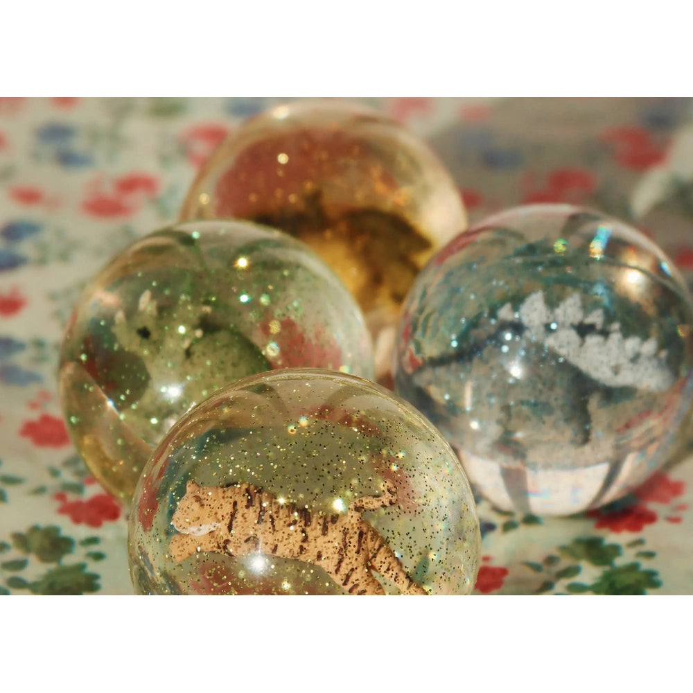Konges Slojd Glitter Bouncing Ball Set Dino: four transparent glitter balls with dinosaurs inside on a floral table