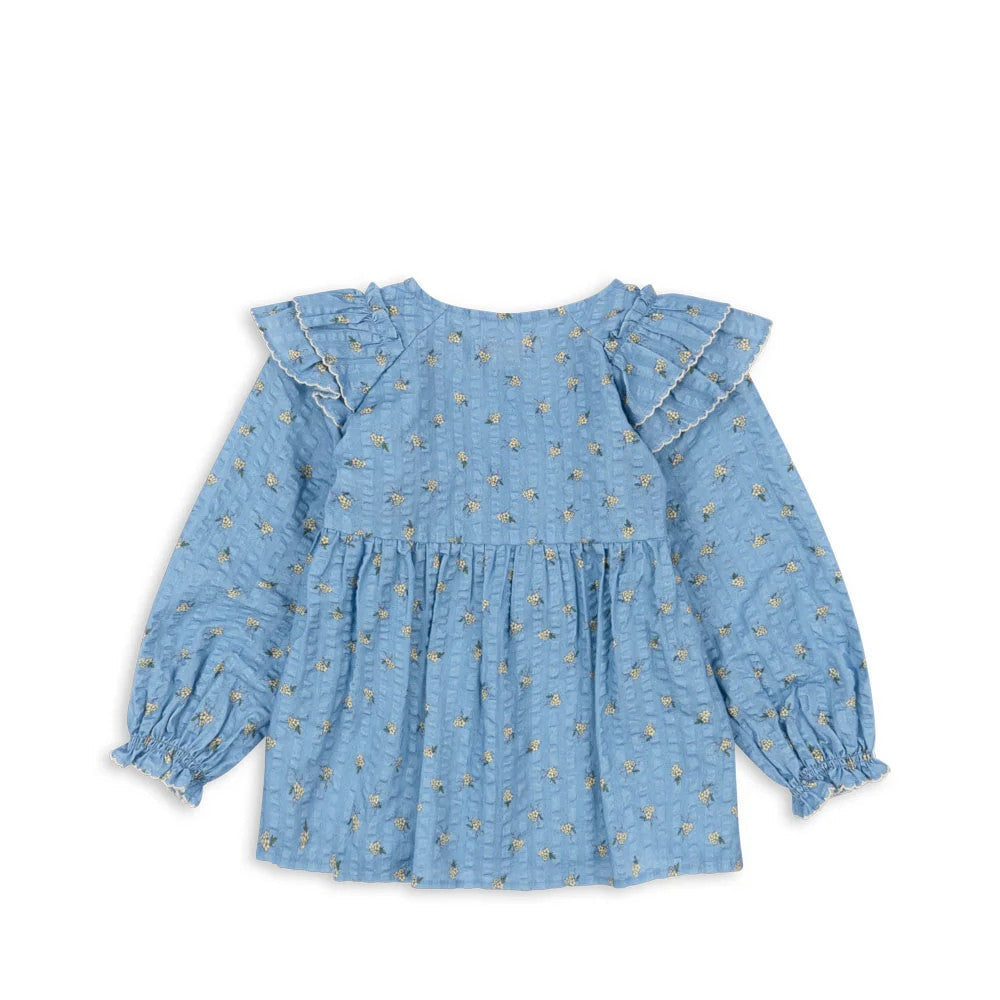 Konges Slojd Kim Frill Blouse Billie Blue, blue floral baby top with ruffled sleeves and gathered waist laid flat.