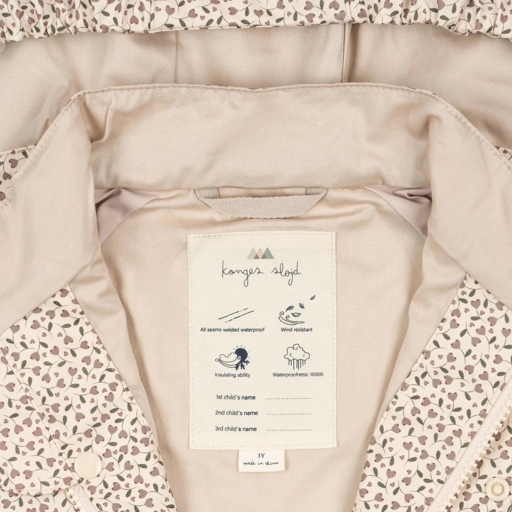 Konges Slojd Rainy Palme Set Milk Tank jacket opened to reveal tag: welded waterproof seams, wind resistant, insulating, 10000mm waterproof.