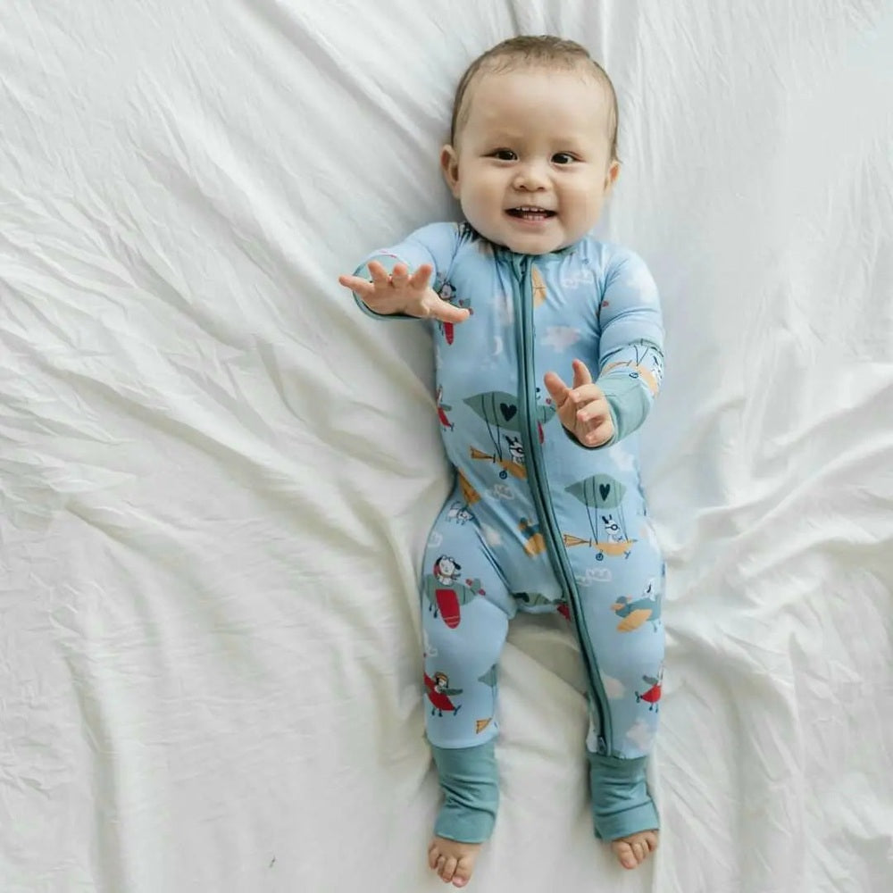 Littlesleepies Fly Away With Me Bamboo Viscose Zippy, light-blue baby onesie; baby reaches forward on white sheets.