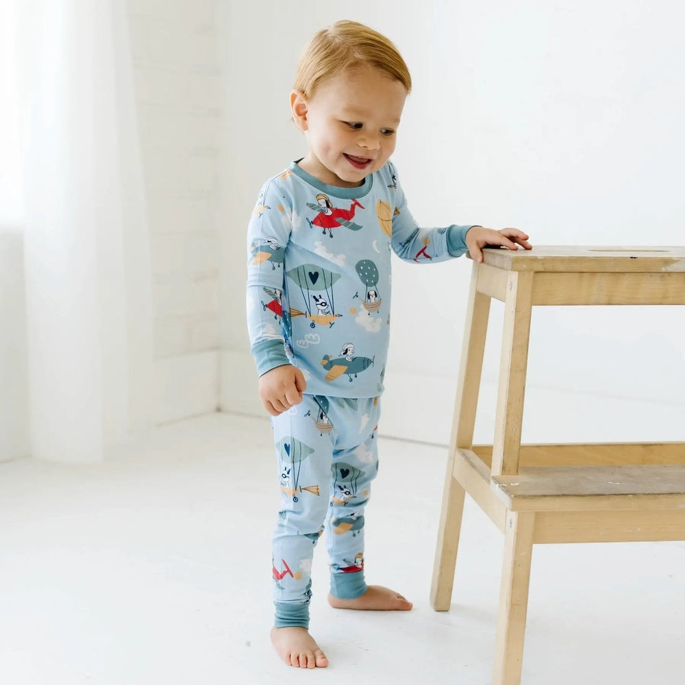 Littlesleepies Fly Away With Me bamboo viscose toddler pajamas in light blue; child stands barefoot beside a wooden stool, parachute print.
