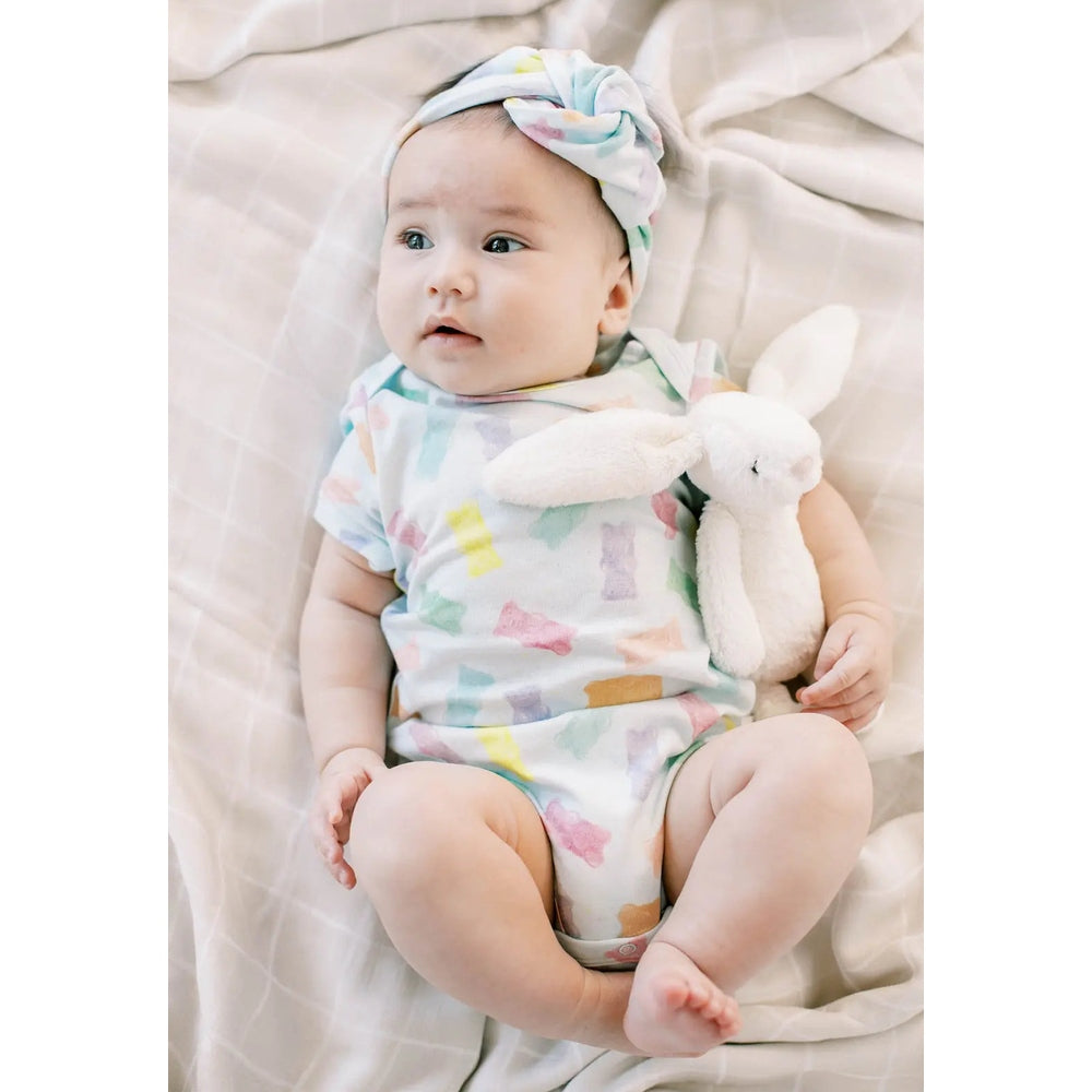 Loulou Lollipop Baby Bodysuit Gummy Bears in pastel print; baby with matching headwrap cuddles a plush white bunny.