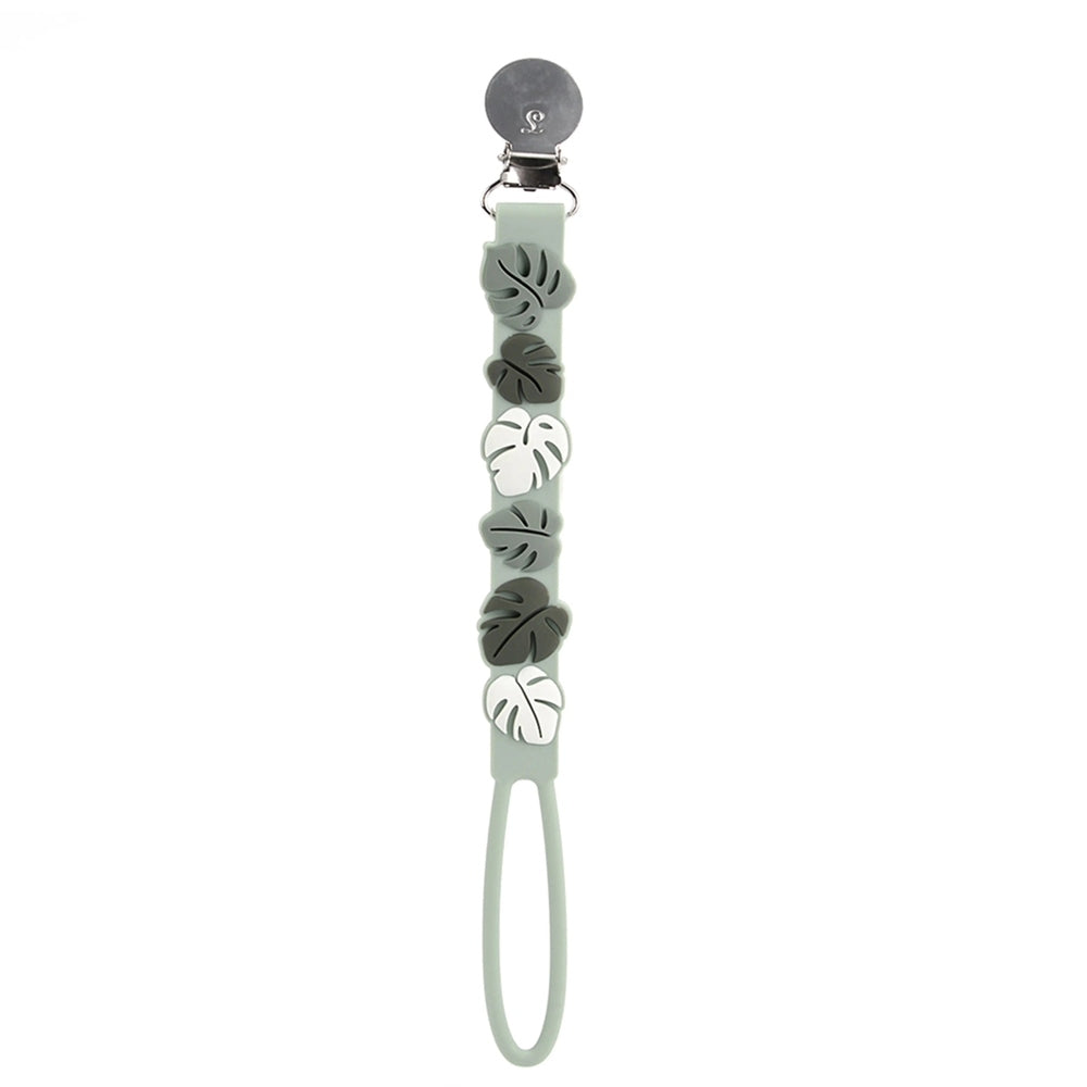 Loulou Lollipop Beadless Pacifier Clip in sage green with gray and white monstera leaf beads, clip securing to clothing.