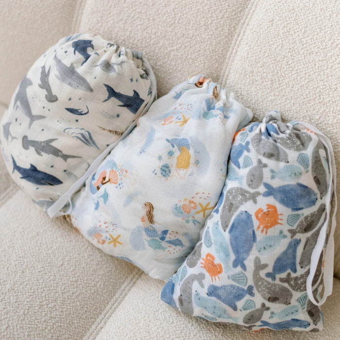 Loulou Lollipop Muslin Fitted Crib Sheet Jungle Friends: three blue-gray jungle-print muslin bags with drawstrings resting on a beige sofa.