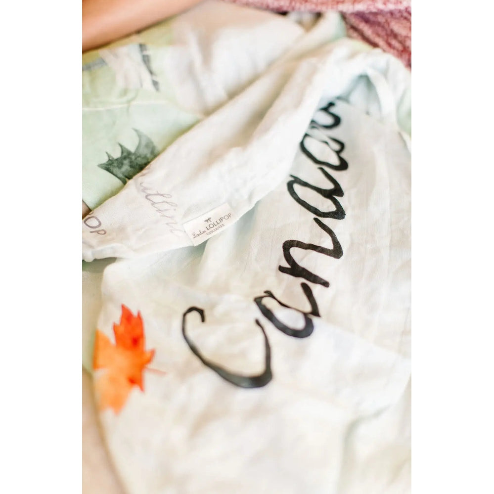 Loulou Lollipop Muslin Swaddle white cotton with bold black script logo; tag visible as it rests in soft folds.