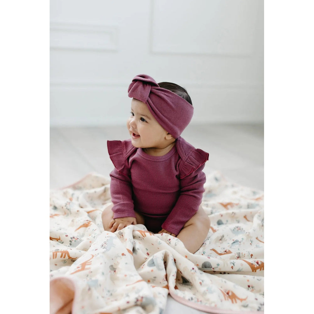 Loulou Lollipop Waffle Knotted Headband Sugar Plum on a smiling baby in burgundy, sitting on a patterned blanket.