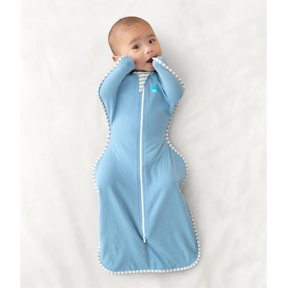 Love To Dream Swaddle Up Original Cotton 1.0 Tog Dusty Blue; baby swaddled in blue with zipper front and striped trim, arms up.