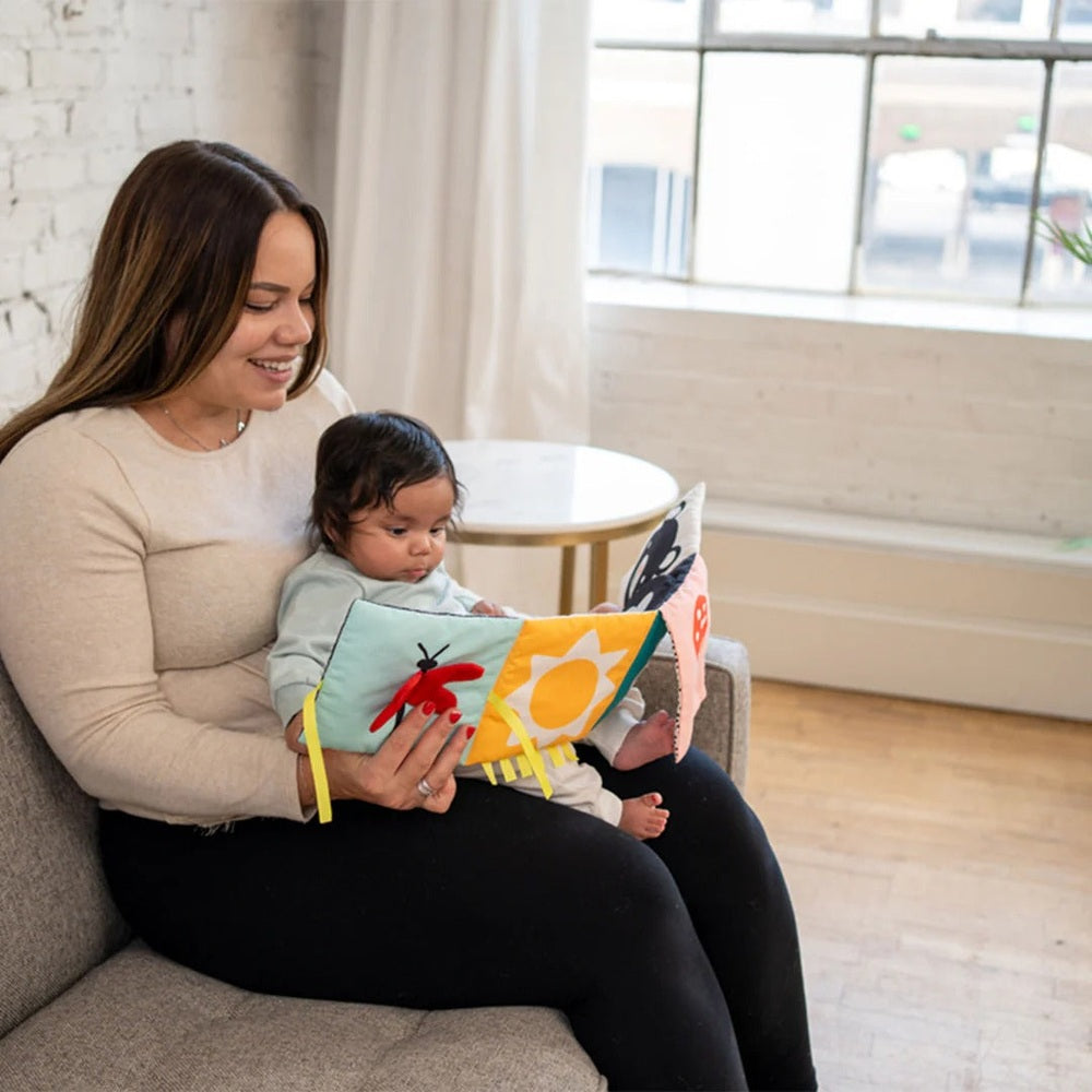 Manhattan Toy Wimmer Seek & Peek Book read by mother and baby on a sofa, pages with colorful shapes.