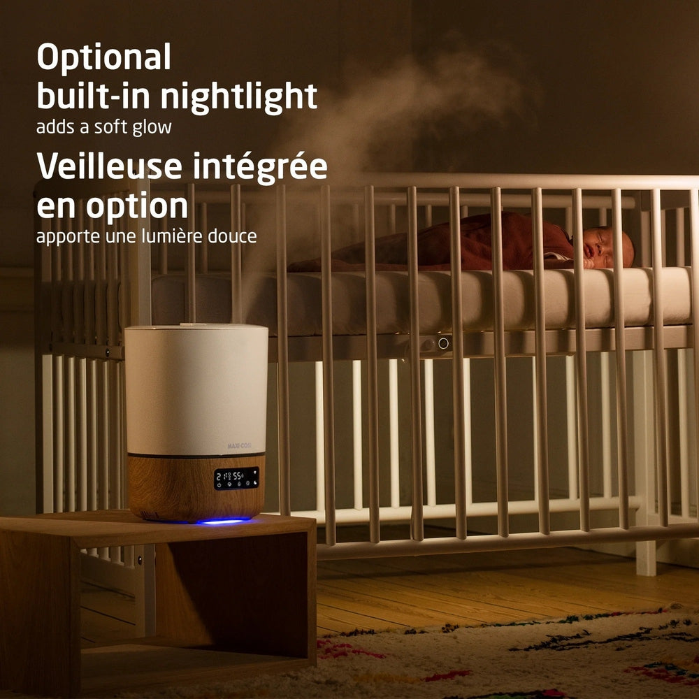 MAXI COSI Smart Humidifier, white with wood base, releasing soft mist beside a nursery crib.