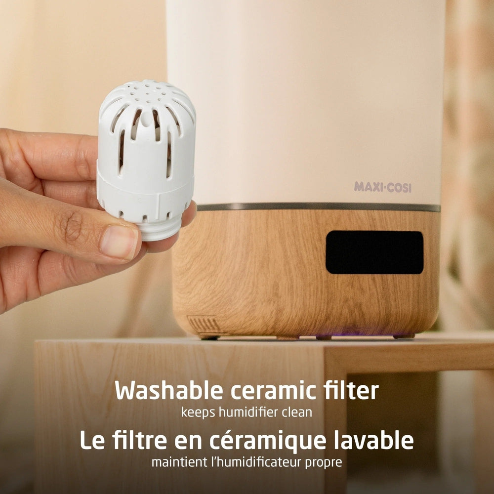 MAXI COSI Smart Humidifier in beige wood finish with a hand inserting a washable ceramic filter.