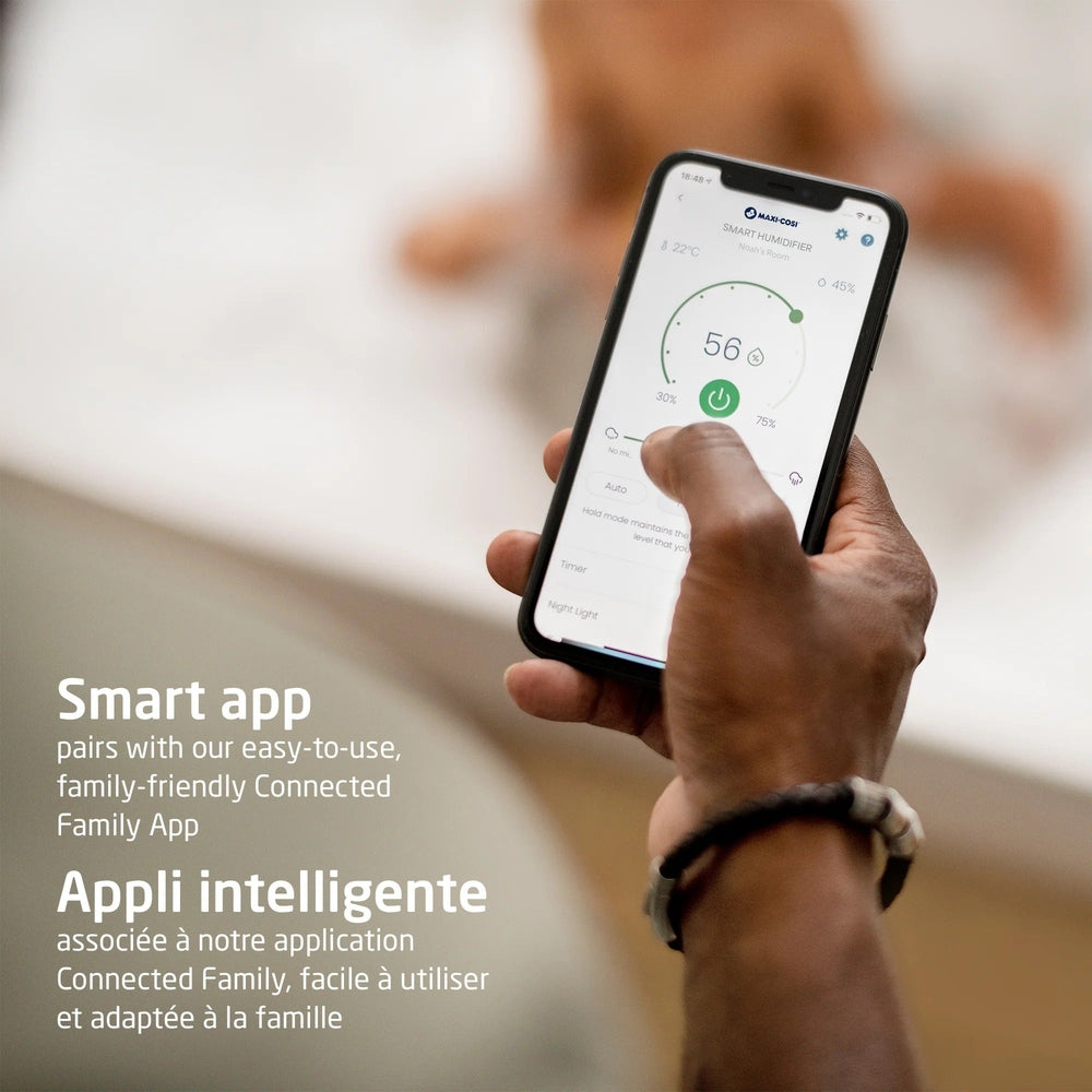 MAXI COSI Smart Humidifier; a hand holds a smartphone showing the smart app, signaling a cozy, healthy home.
