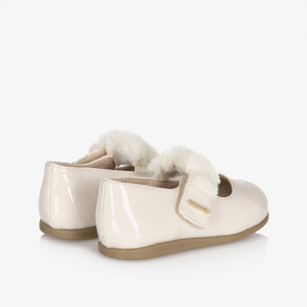 Mayoral Girl Patent Leather Mary Janes in cream with fluffy lining, Velcro straps fastened on a toddler’s feet.