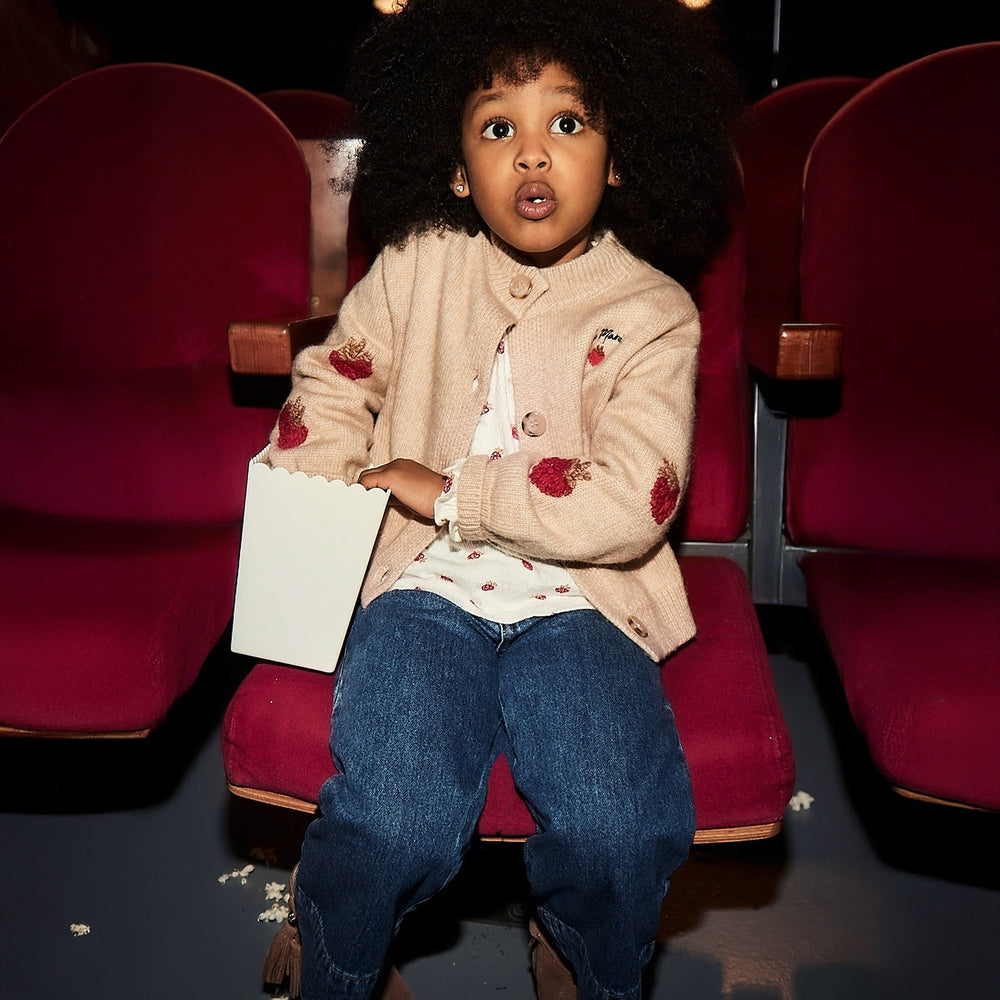 Mayoral Wide Leg Denim Pants worn by a toddler girl in a beige cardigan at the cinema, showcasing loose blue denim legs and popcorn.