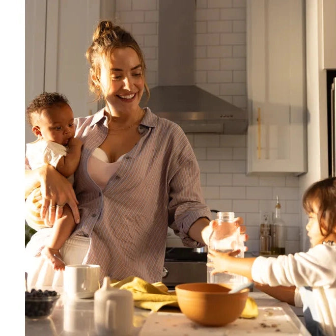 Medela Motion Inbra Double Electric Breast Pump; mom in a bright kitchen pumps while cradling her baby.