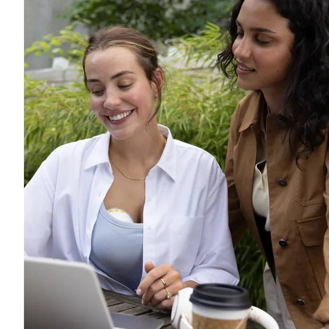 Medela Motion Inbra Double Electric Breast Pump lifestyle shot with two women outdoors, smiling over a laptop.