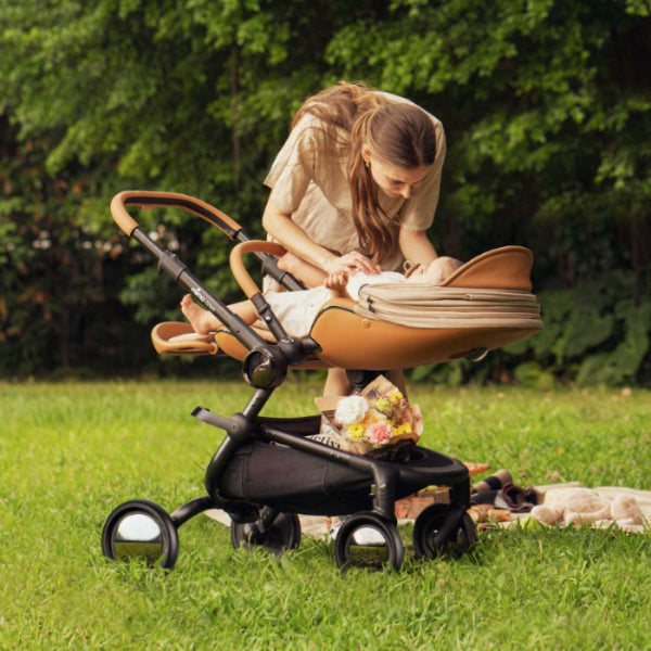 Mima Creo Stroller with tan bassinet on a black frame as a parent adjusts the bassinet outdoors.