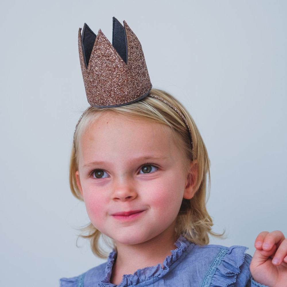 Mimi & Lula Glitter Crown Alice Gold headband on a smiling toddler wearing a blue frilled top