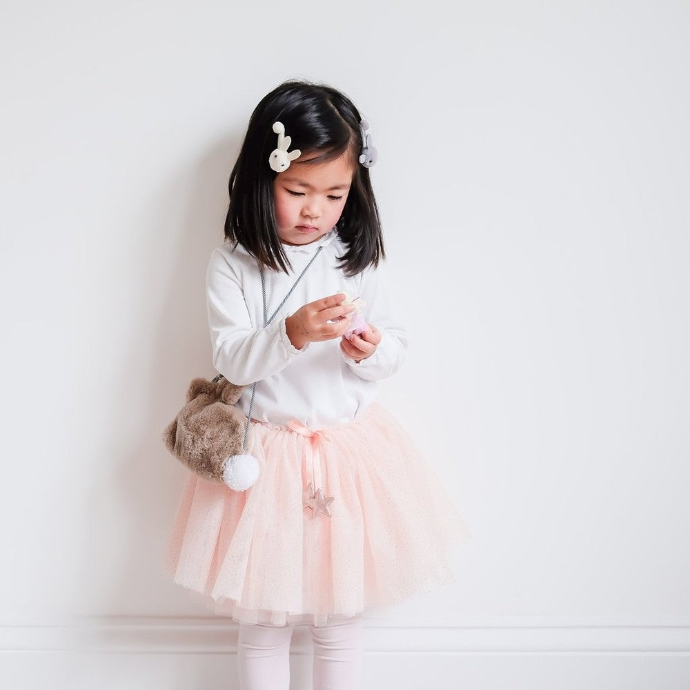 Mimi & Lula pink tutu for toddlers in soft tulle; girl in white top with beige pom-pom bag