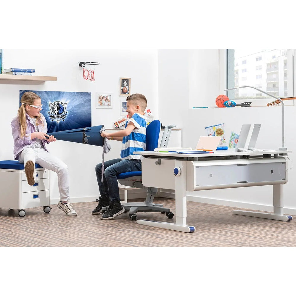 MOLL Champion Height Adjustable Desk Right Up, white with blue feet; kids work at it in a bright study room.