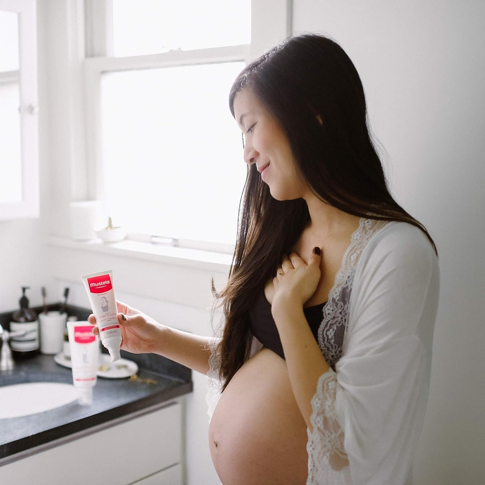 Mustela Bust Firming Serum 75 ml in red‑white tube held by pregnant woman in a bright bathroom