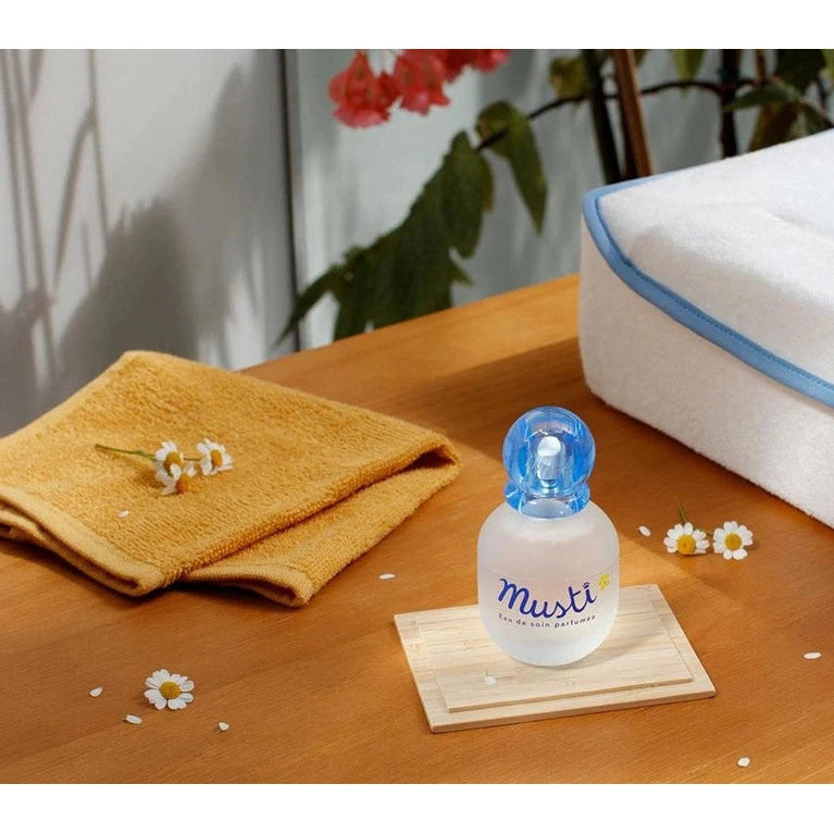 Mustela Musti Perfumed Treatment Water 50 ml bottle with blue cap on a wooden tray beside a towel