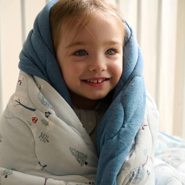 Nest Designs Bamboo Jersey Cozy Blanket Medium Snowy Snuggles wrapped around a smiling toddler in a soft blue blanket.