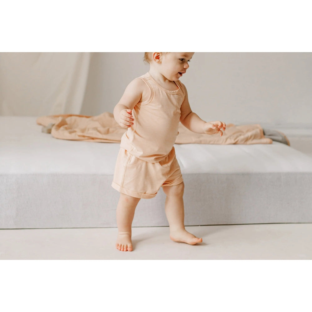 Nest Designs Bamboo Jersey Shorts Pantone Bellini; a baby in peach loungewear walking on a light floor.