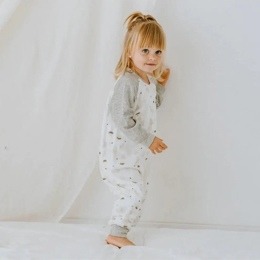 Nest Designs Bamboo Long Sleeve Footed Sleep Bag 1.0 Tog, white with grey sleeves; toddler standing on a bed.
