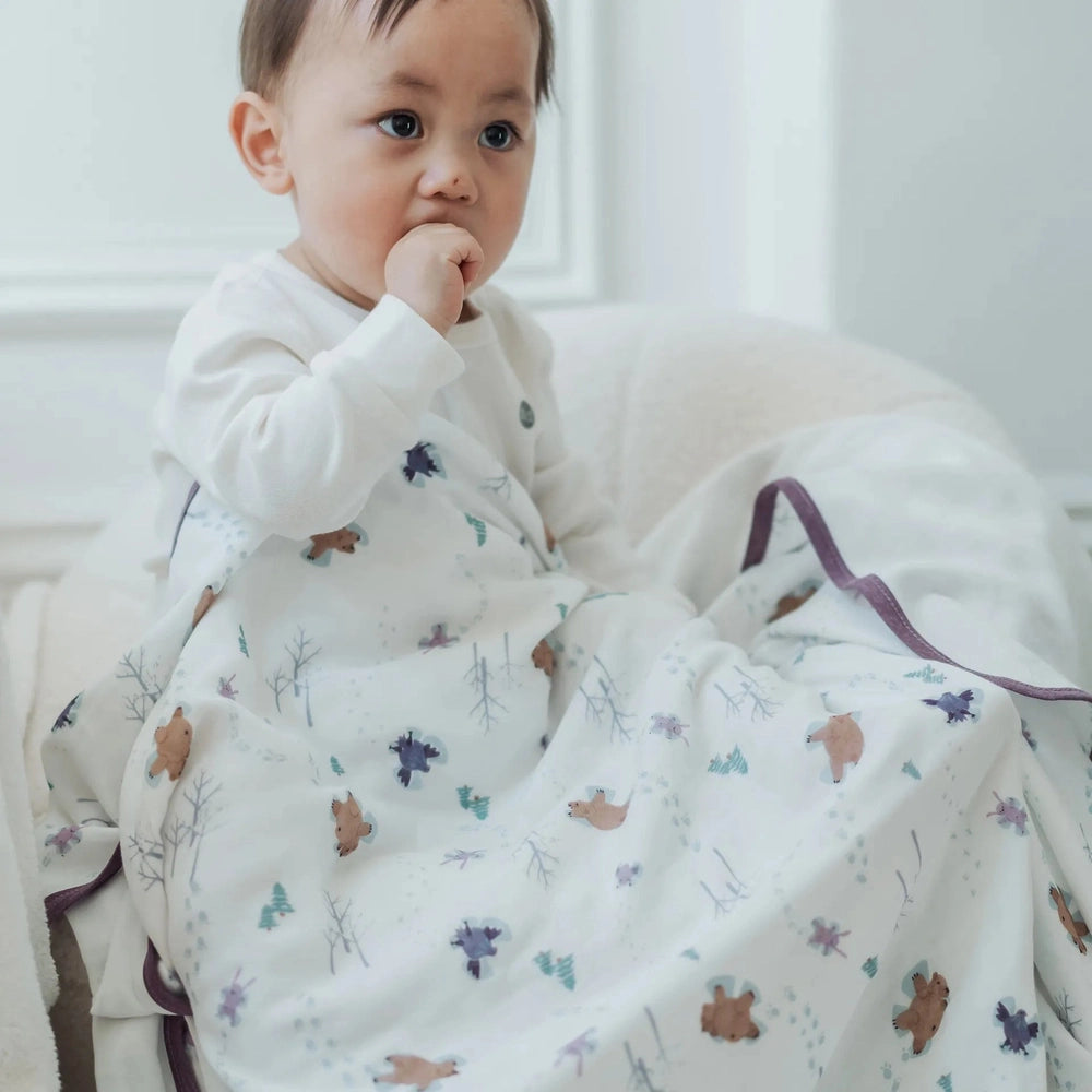 Nest Designs Bamboo Muslin Small Nesting Blanket 120cm x 120cm swaddles a baby on a white couch, showing breathable fabric and cozy wrap.