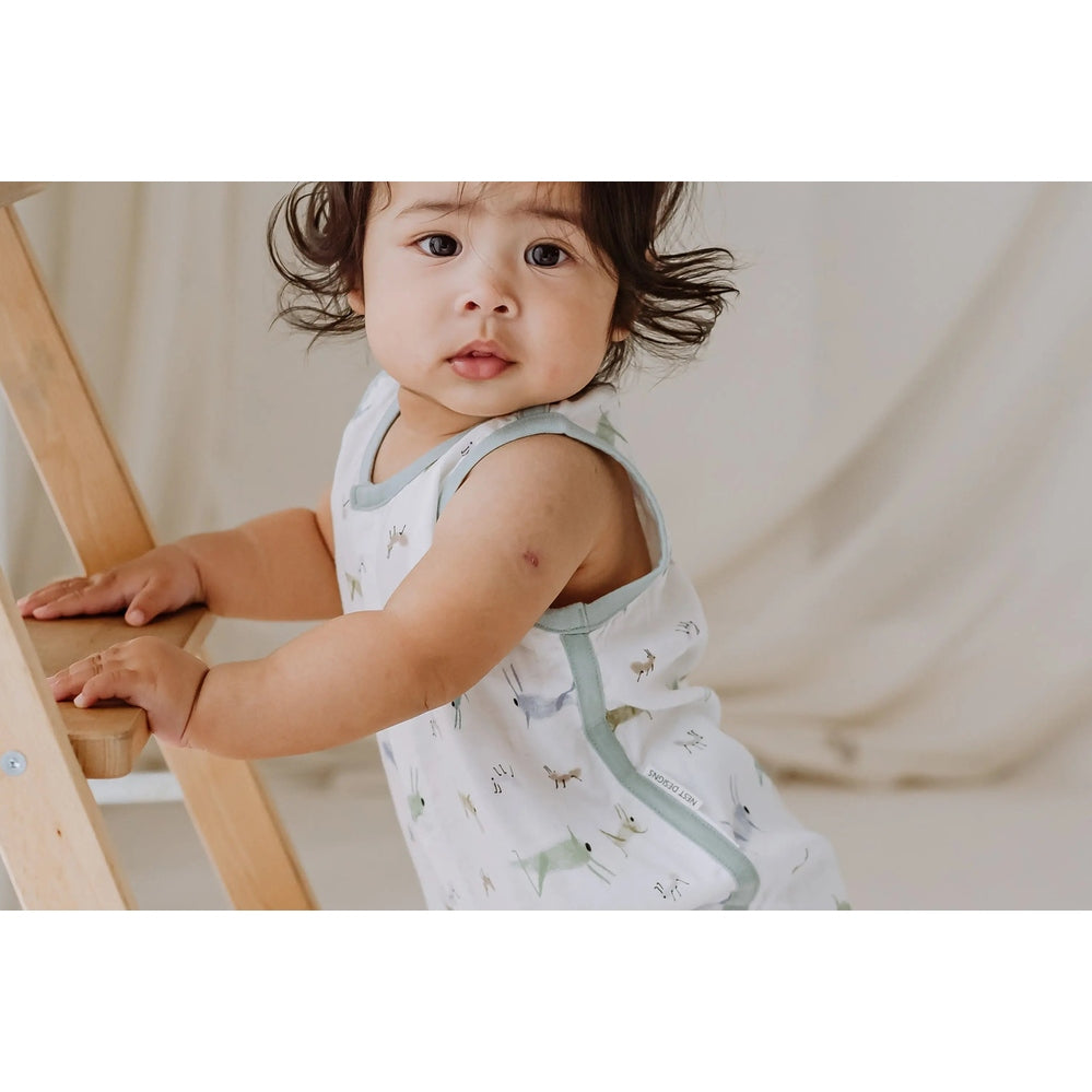 Nest Designs Bamboo Pima Sleeveless Onesie The Ant & The Grasshopper; baby stands gripping a wooden ladder, showing pale gray trim.